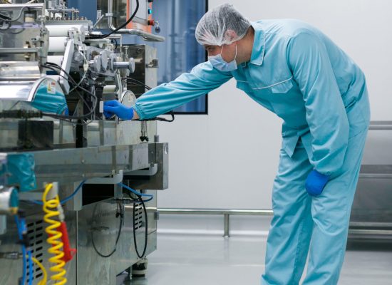 vertical picture of bended caucasian scientist in blue lab suit trying to fix manufacture machine with shafts in clean factory